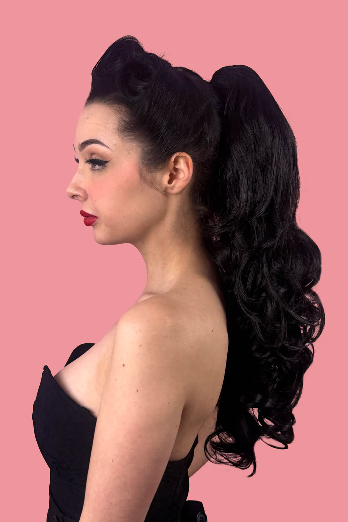 Woman in a black dress with red lipstick against a pink background. Long wavy ponytail hairpiece extension: Tiffany black 1B