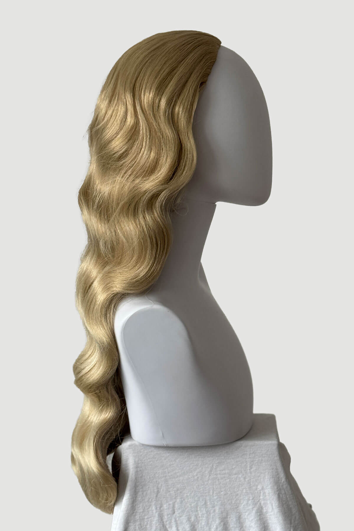 Mannequin head with long, blonde hair styled in a ponytail on a plain background. Ultra long half wig with hollywood waves. ash blonde and light blonde 613T24