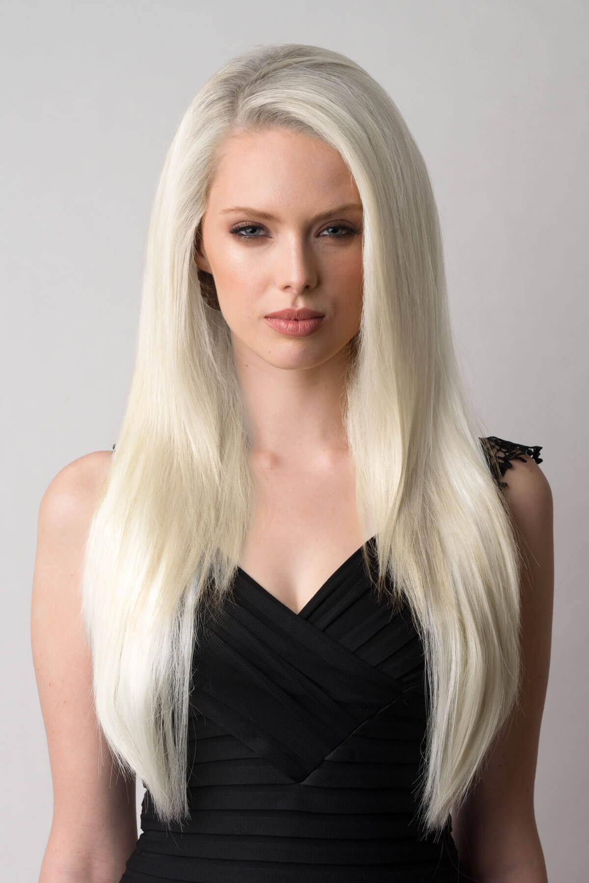 Woman with long blonde hair wearing a black dress against a gray background. Straight platinum blonde half wig hairpiece (3/4 wig): Shannon