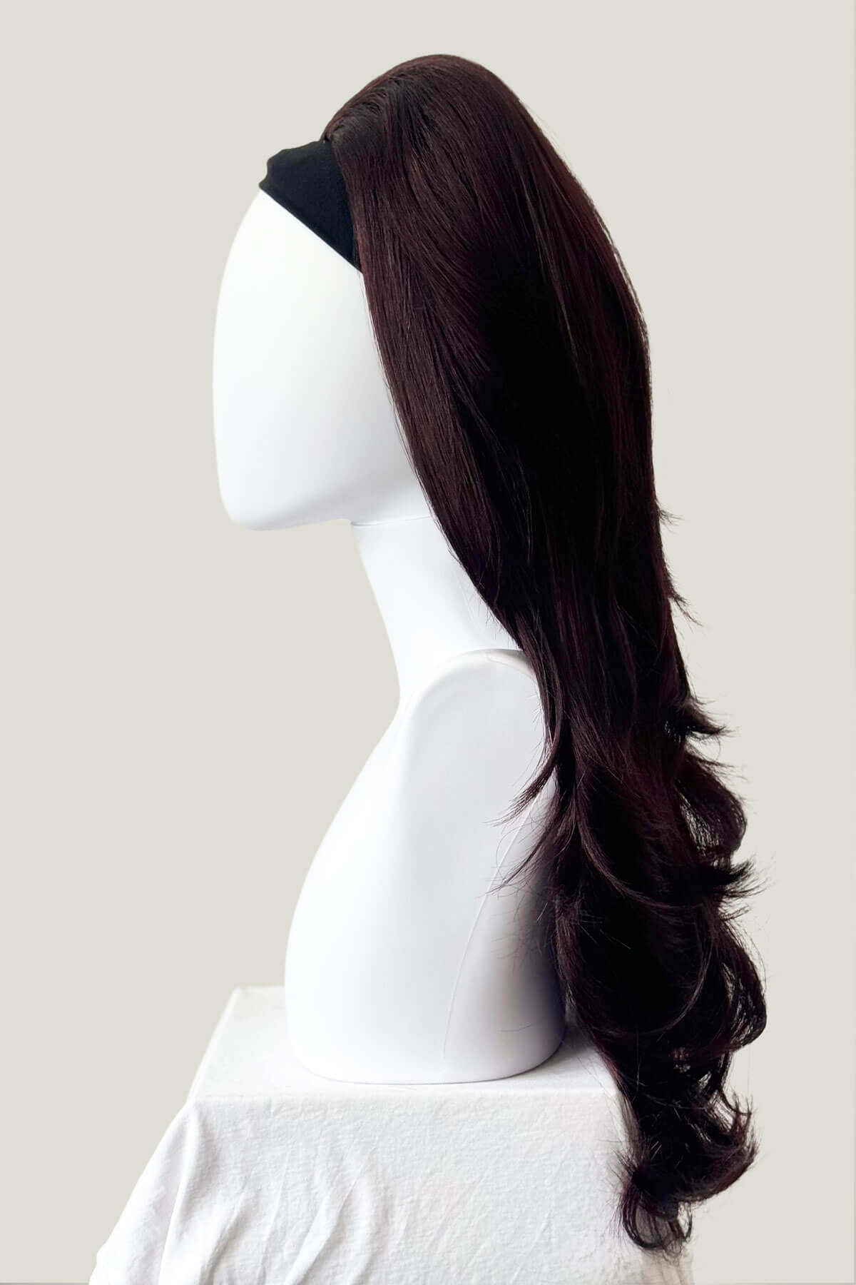 Dark brown hair extension on a mannequin head against a plain background. Black & purple half wig hairpiece, wavy, loose curls: Indira