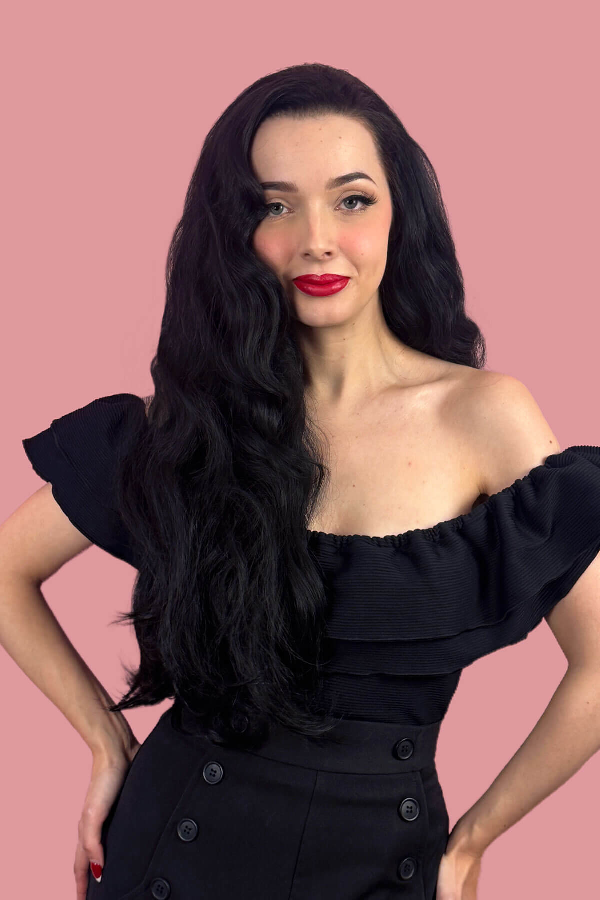 Woman with long black wavy hair and red lipstick posing against a pink background. Black half wig hairpiece (3/4 wig), long layers: Aislynn black 1B