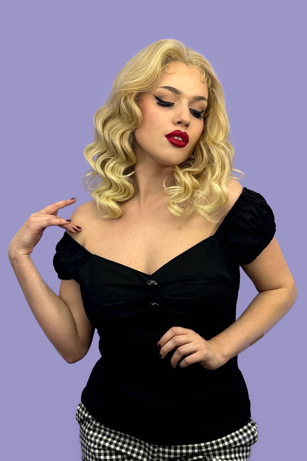 Woman wearing a black top with short sleeves against a purple background. Blonde pinup wig, lace front: Irina blonde 613T24