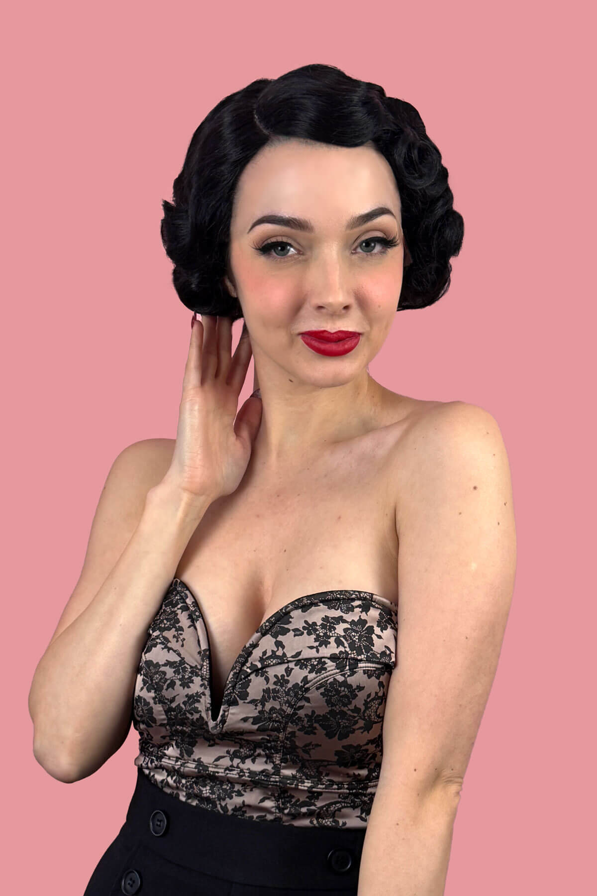 Woman with short black wavy hair against a pink background. Black lace front wig, short with finger waves: Viola
