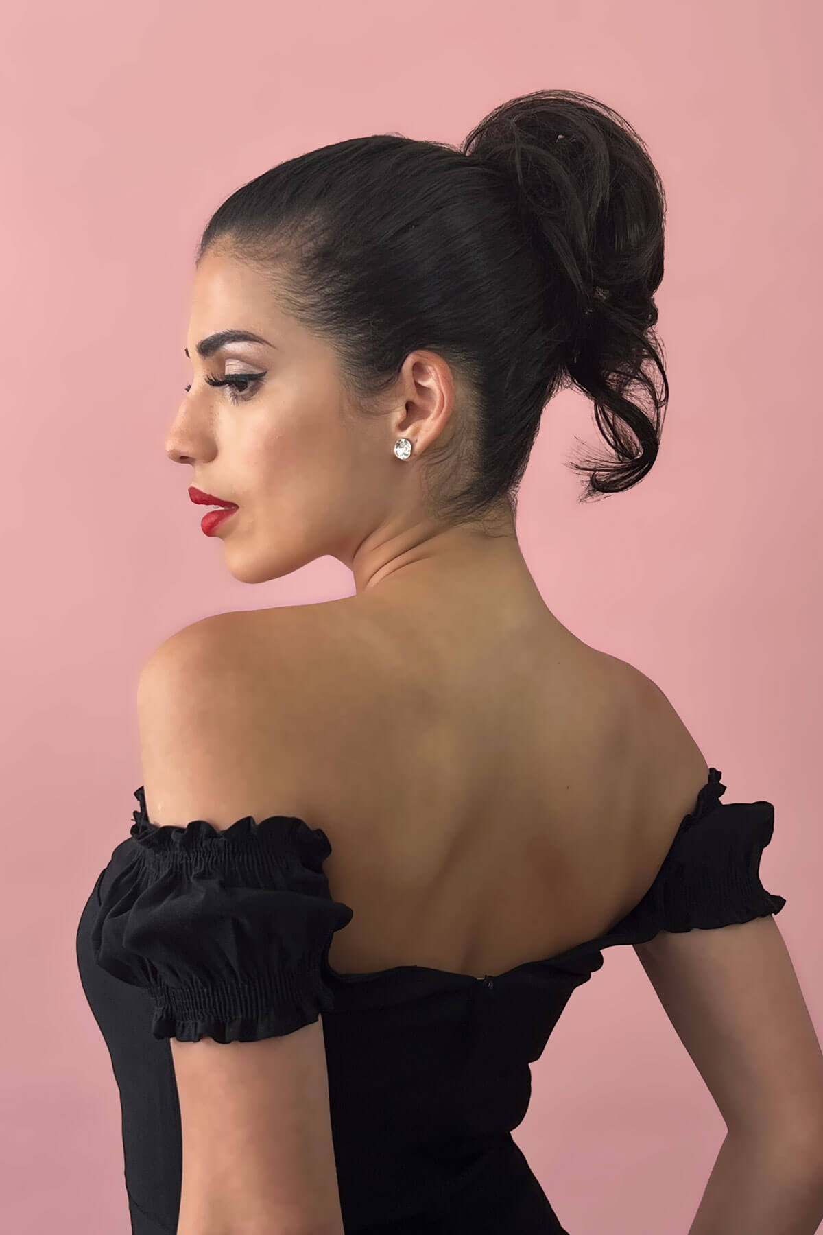 Woman in a black off-shoulder dress with a pink background. Short ponytail extension hairpiece, short with whisps: Leah black 1B