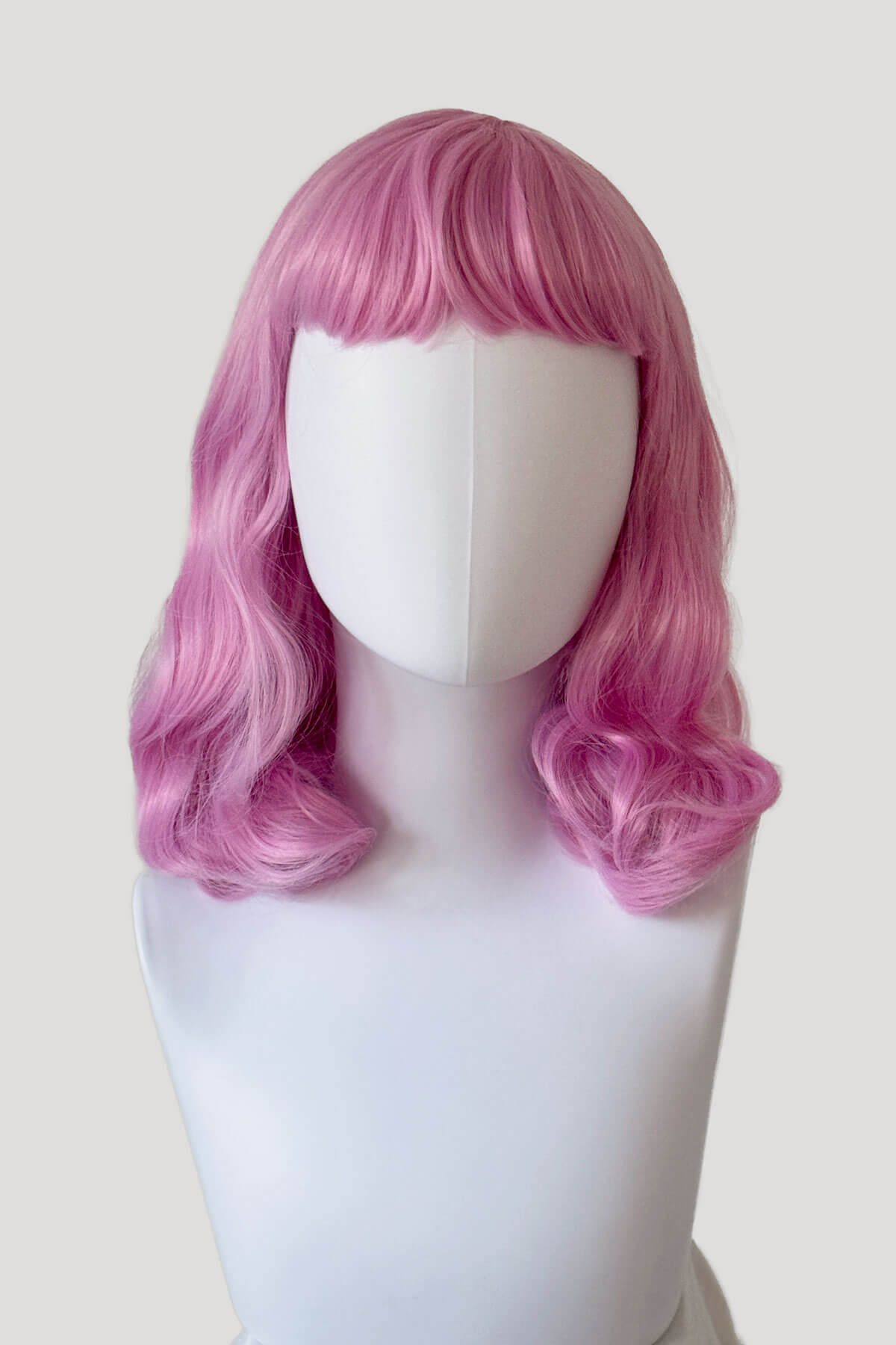 Pink wig on a mannequin head against a white background. Pink pinup style wig, with finger waves and a short fringe, 1950s style: Stevie light pink 2614