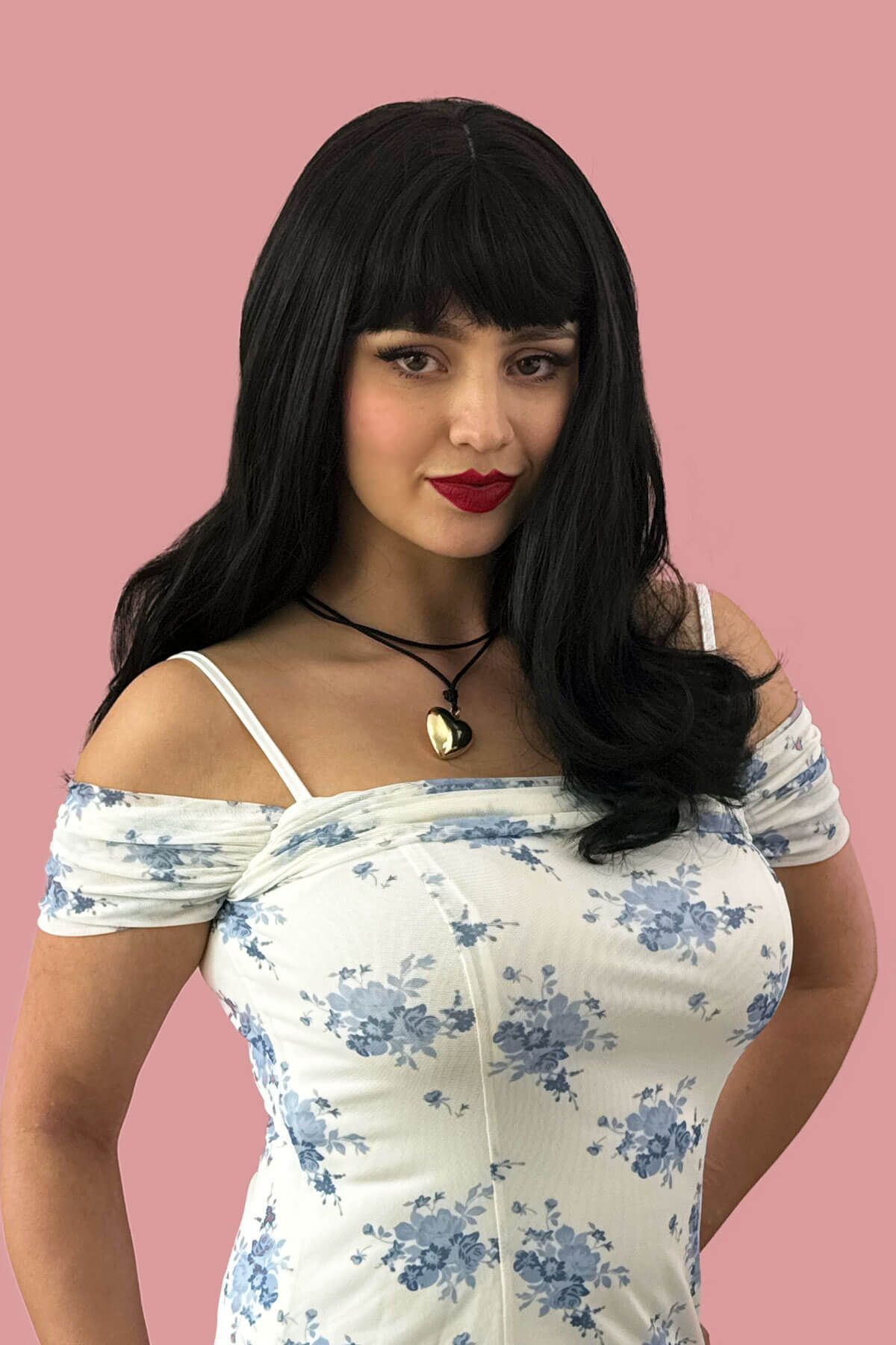 Woman wearing a floral dress with a plain background. Long black wavy bob (LOB) wig with straight retro fringe: Ciarra