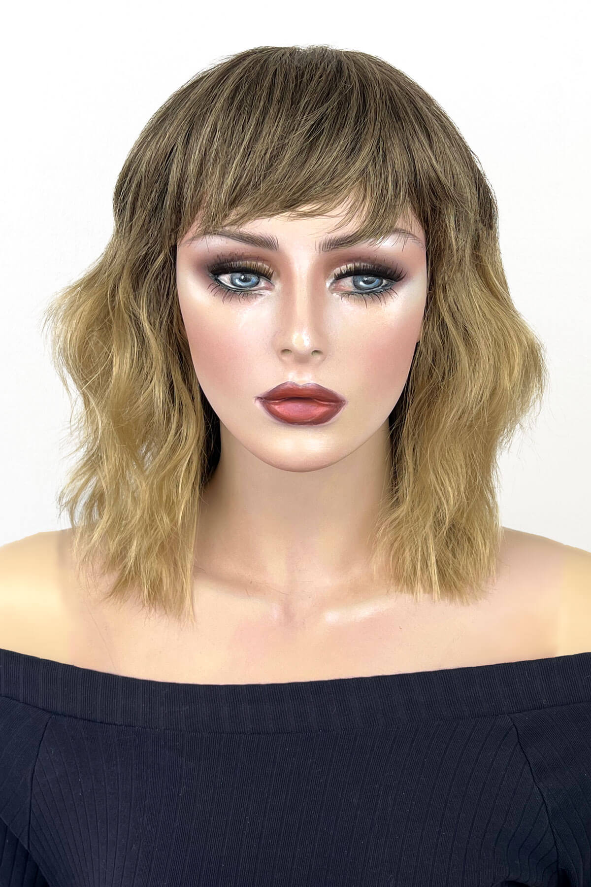 A shoulder-length wavy wig with bangs in a light brown and blonde ombre style, modelled on a mannequin head against a plain white background. Long dark brown bob wig (LOB) with textured waves: Anais 8TN24