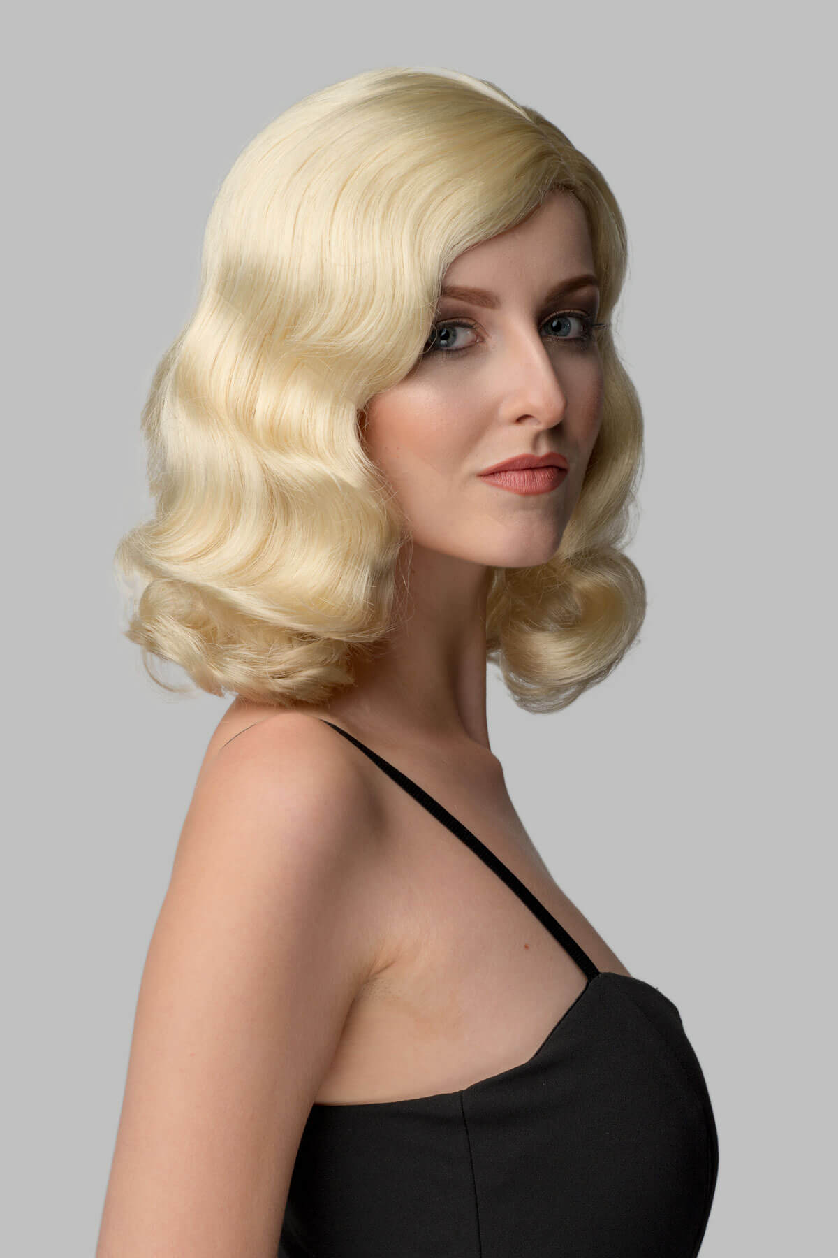 Woman with styled blonde hair against a gray background. 40s blonde pinup style wig with marcel waves: Lauren