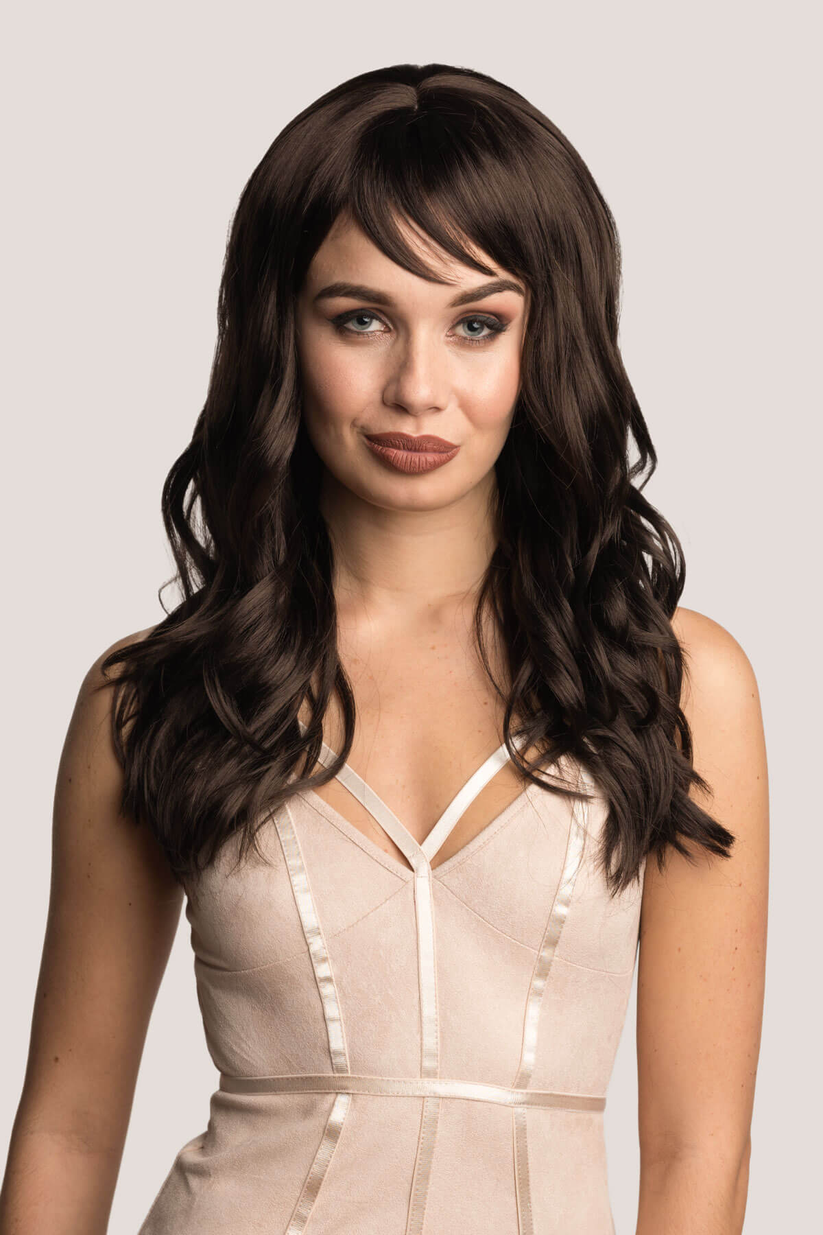 Woman with long wavy brown hair wearing a beige dress against a plain background. Long brown wig with gentle waves: Emma
