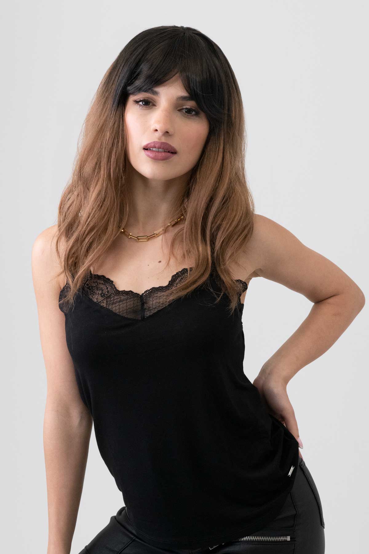 Woman wearing a black sleeveless top with lace detailing on a white background. Long wavy bob wig (lob), dark brown to light brown ombre: Rowena