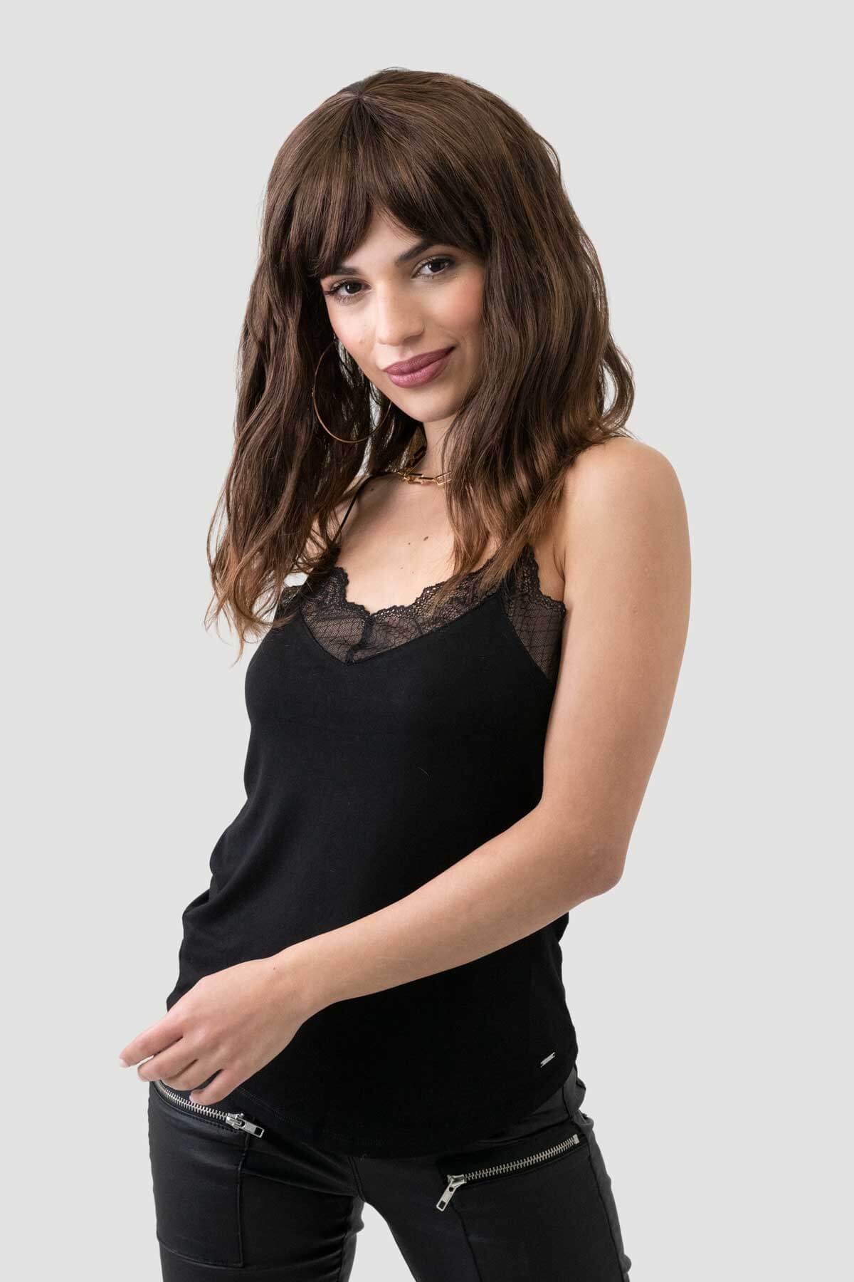 Woman wearing a black sleeveless top with lace detail on a light gray background.  Brown long wavy bob (lob) wig with highlights: Melanie