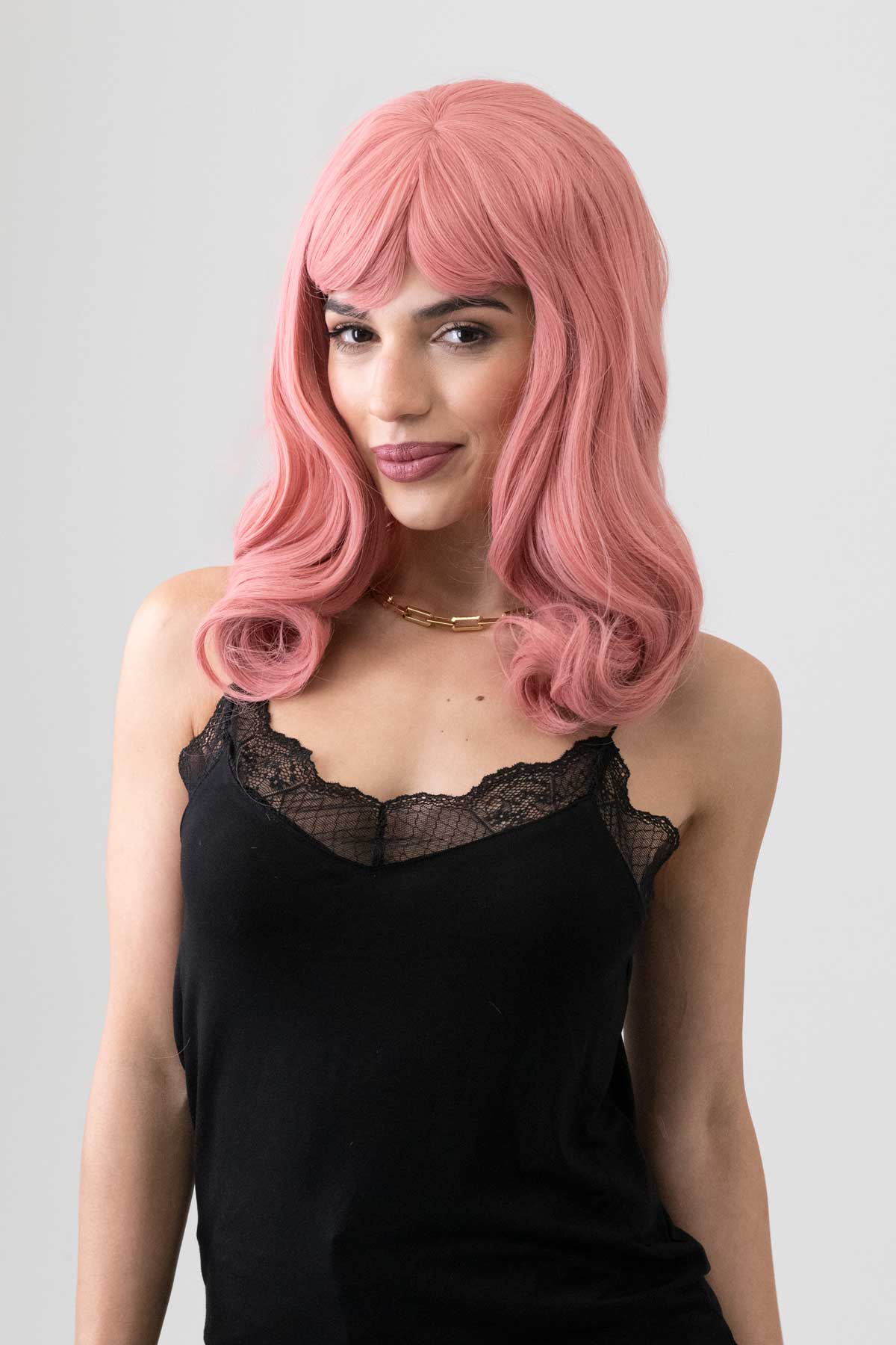 Woman with pink wig wearing a black top on a gray background. Dusty Pink 50s vintage style wig with short fringe: Paloma