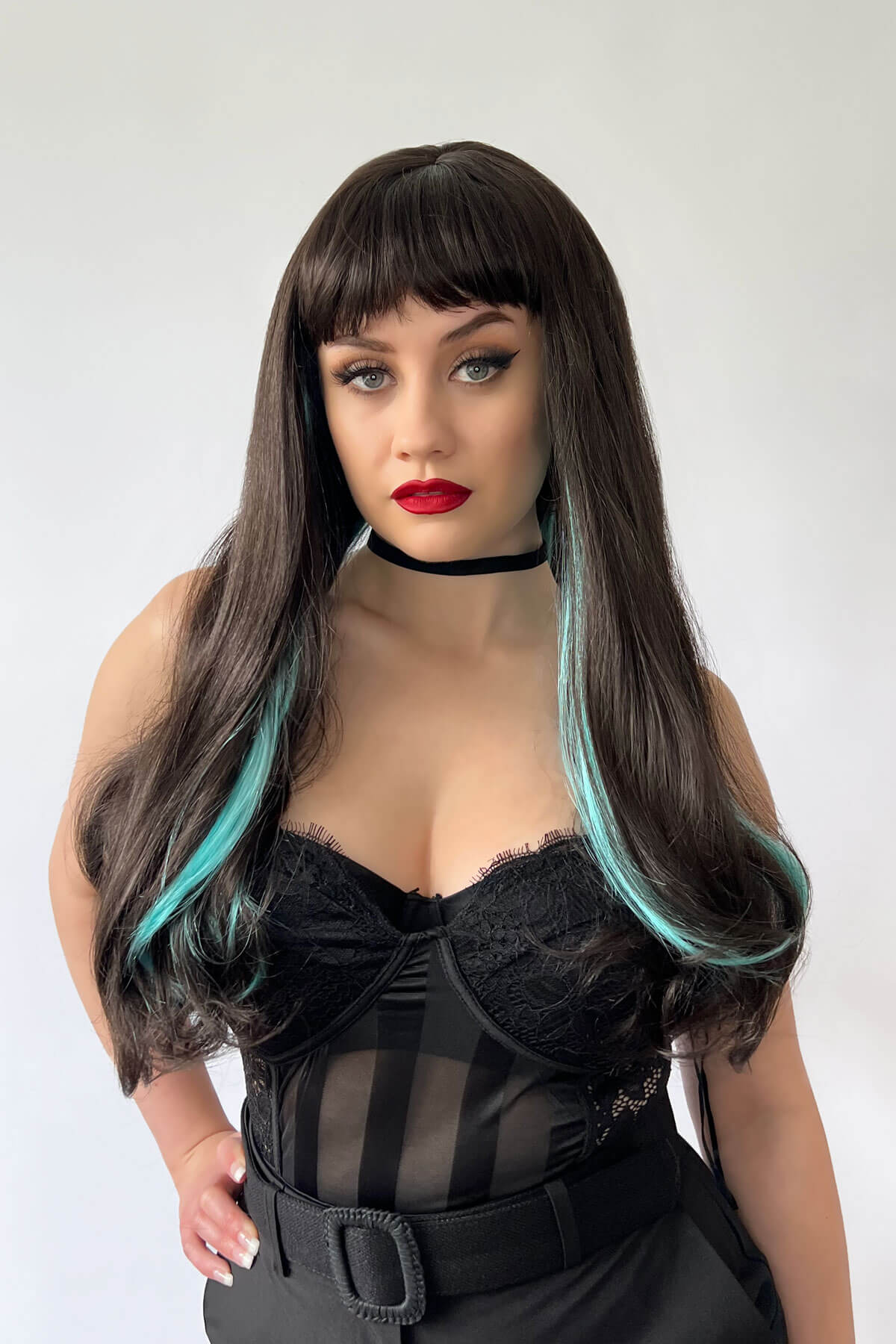 Woman with long dark hair and red lipstick wearing a black lace top against a white background. Long dark brown wig with blue streaks and a straight fringe: Cyane