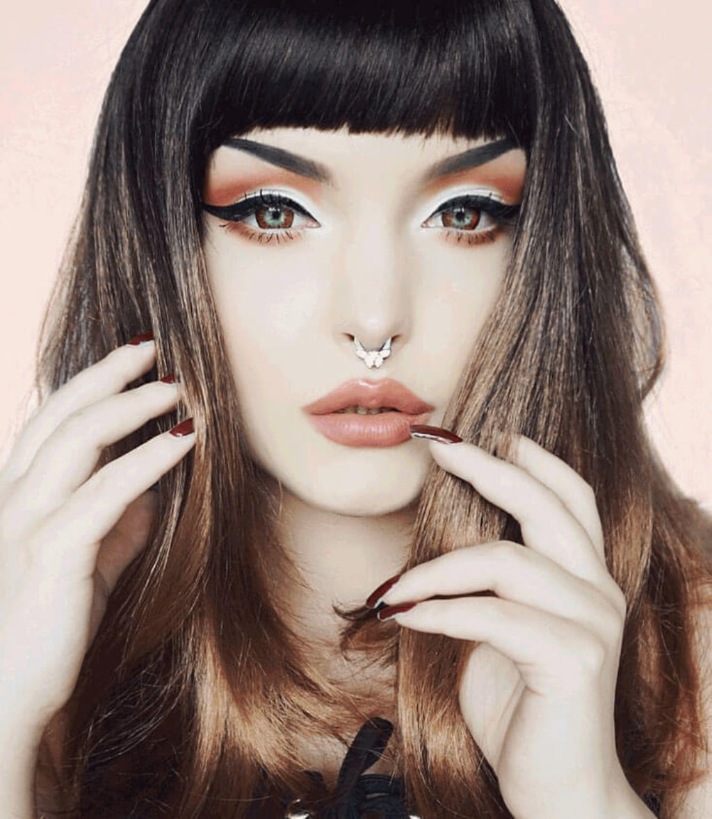 Close-up of a person with dramatic makeup and long hair against a light background. Long bob wig, dark brown blending to light brown: Harper