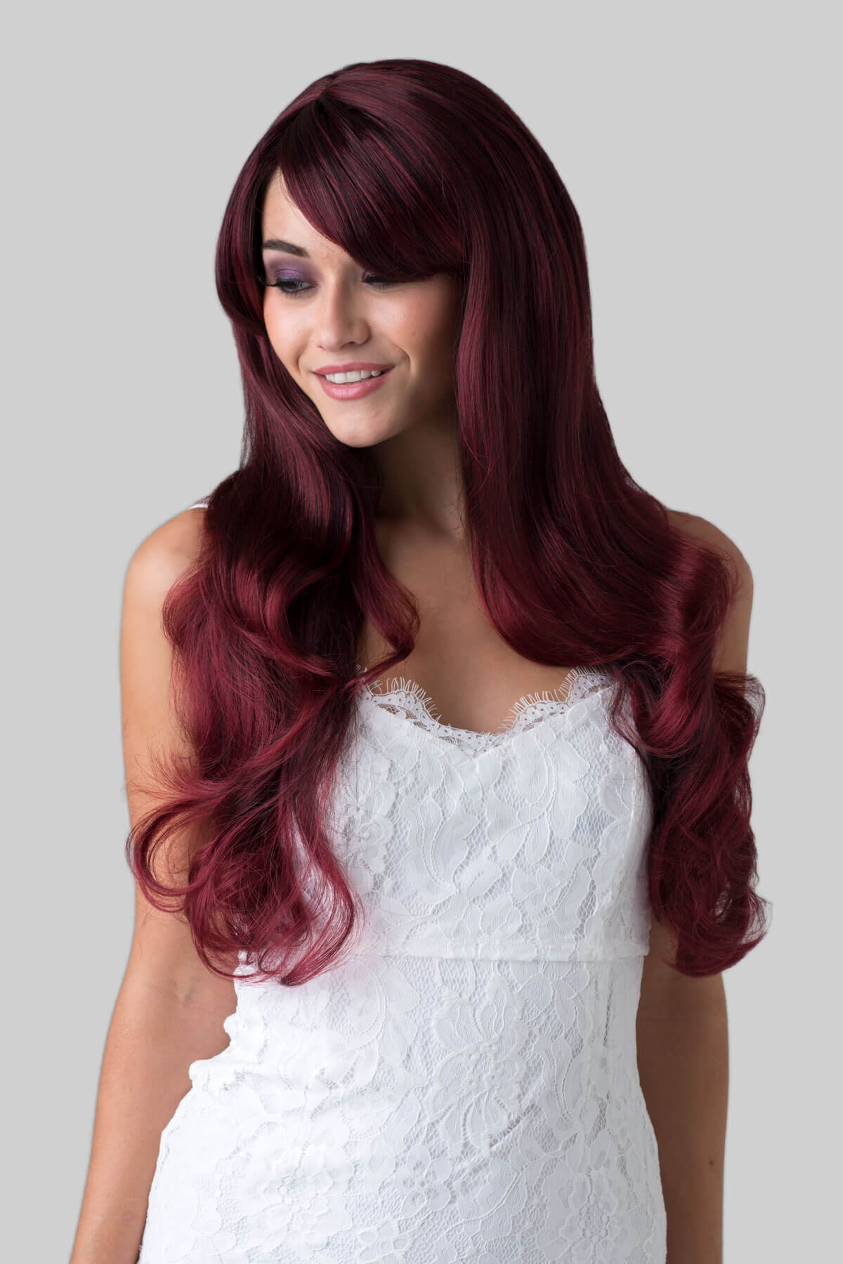 Woman with long burgundy wig wearing a white dress on a grey background. Long red wavy wig with black lowlights: Anji