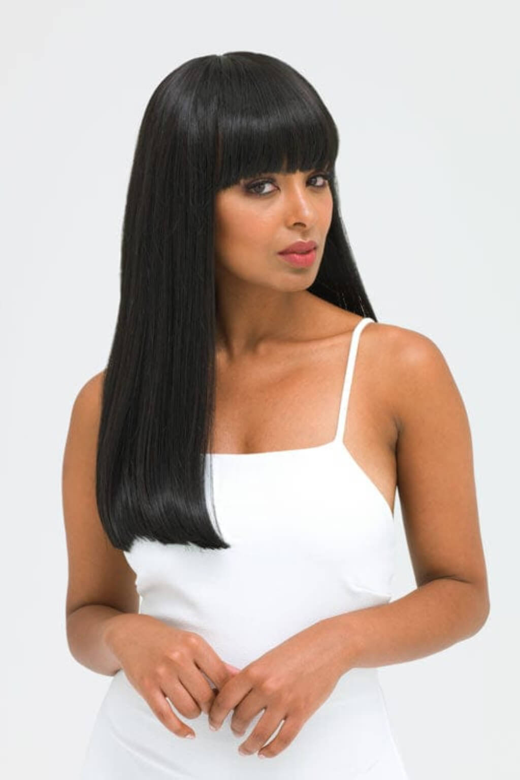 Woman with long straight black hair wearing a white top on a light grey background. Long straight black wig with straight fringe: Carmen