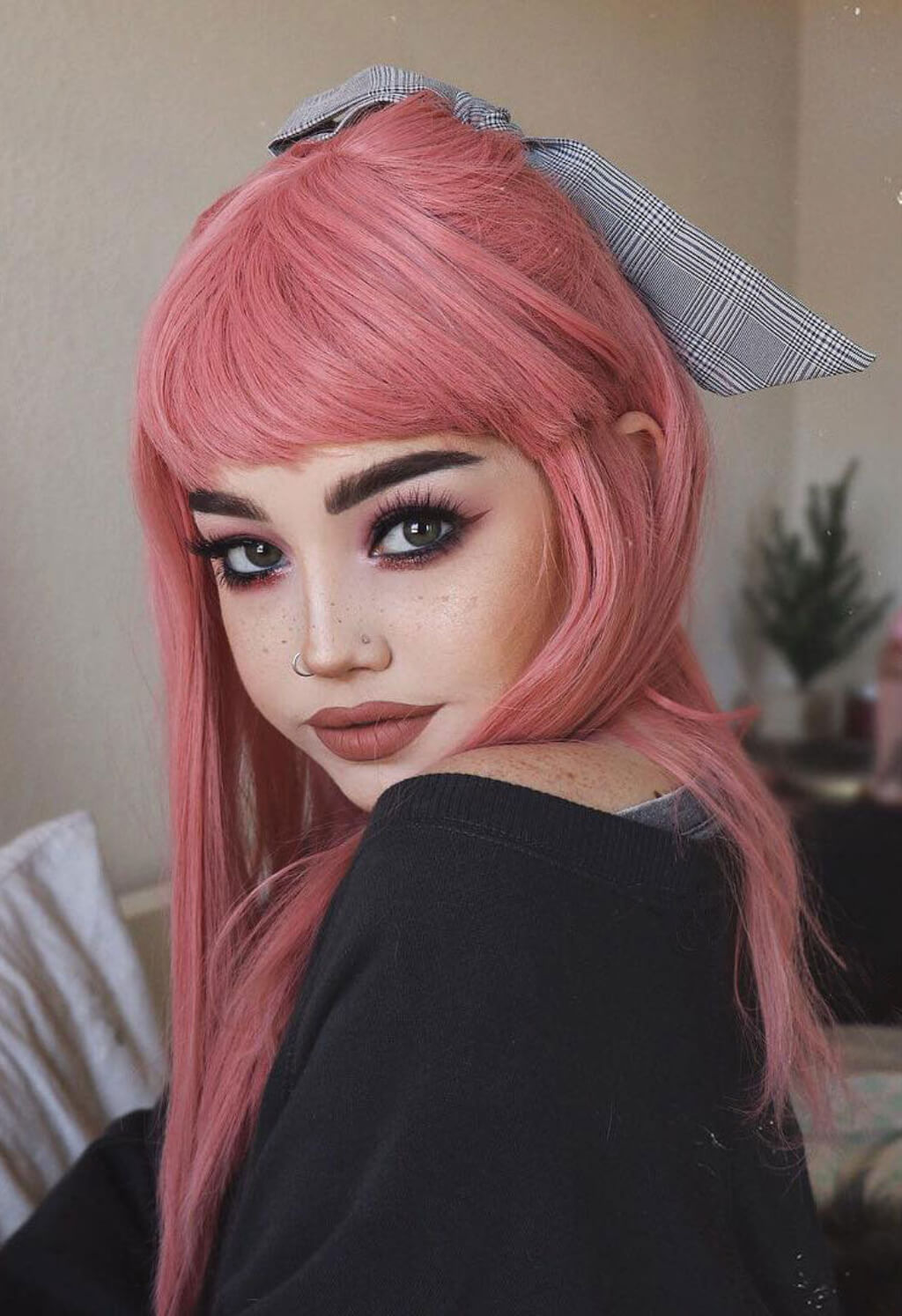 A person with long pink hair, bangs, and a gray plaid bow in their hair, wearing a black top. Long Pink Wig With Short, Straight Fringe: Stephanie