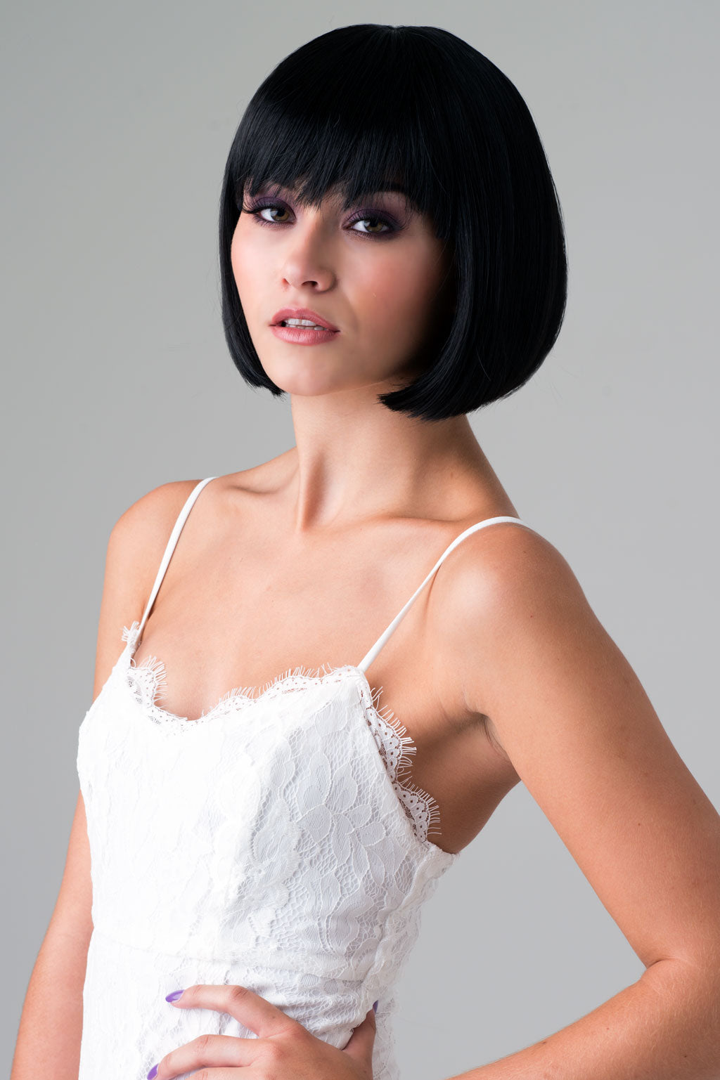 Woman with a stylish black bob haircut wearing a white lace top against a gray background. Short black bob wig: Josie