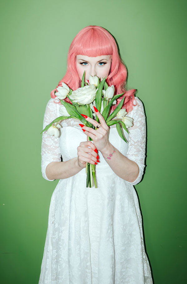 Woman in wedding dress holding flowers with pink wavy hair.